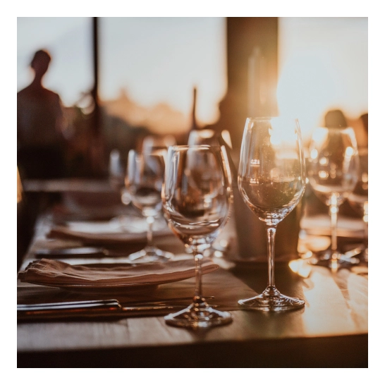Elegant wine glasses on restaurant table with warm sunset lighting and blurred diners in background - Travel in Clifton, NJ
