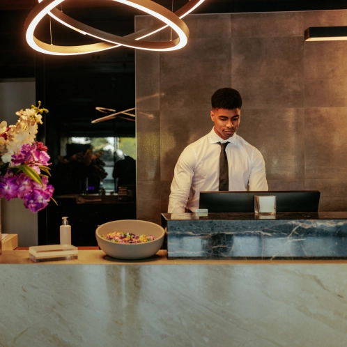 Hotel receptionist in formal attire working at modern marble front desk with decorative lighting and flowers - Travel in Clifton, NJ