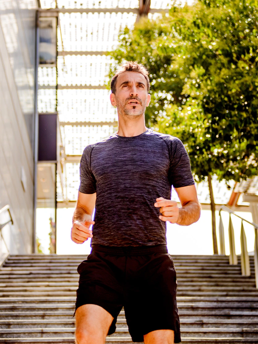 Athletic man jogging outdoors in black shorts and navy shirt on sunny day with urban background - Optilume drug coated balloon dilation in Clifton, NJ