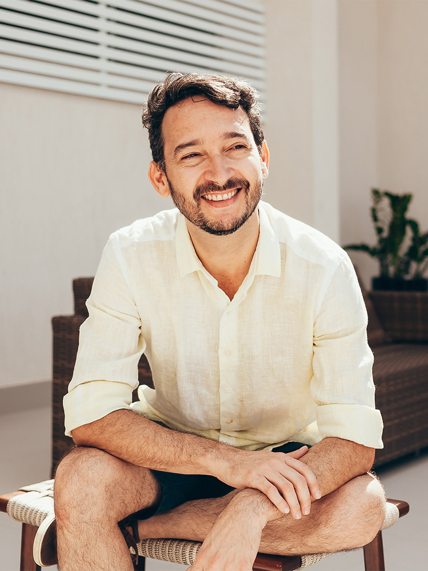 Smiling man in white linen shirt sitting casually in bright, modern interior space - Peyronie disease in Clifton, NJ