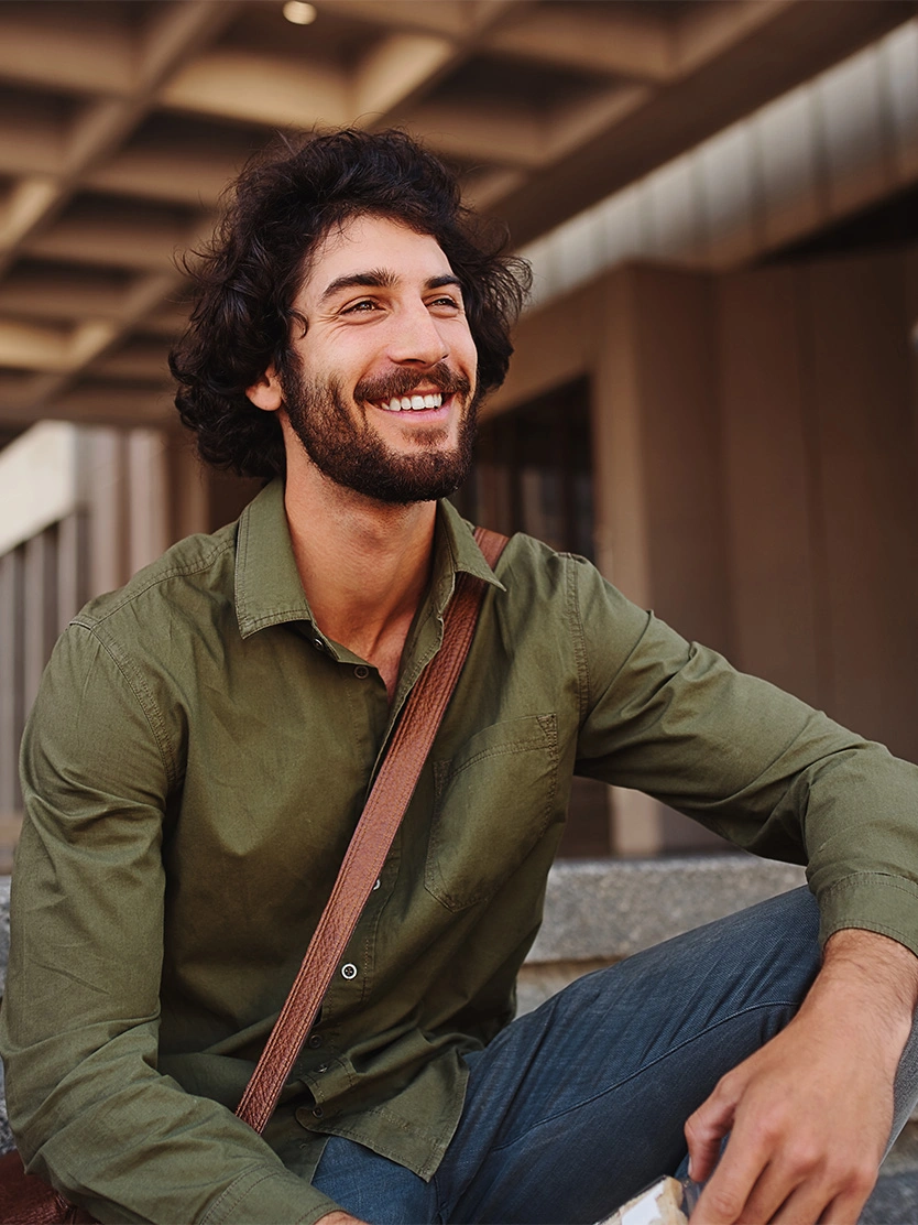 Smiling bearded man in green shirt sitting casually outdoors with brown leather bag strap across shoulder - Stent placement in Clifton, NJ