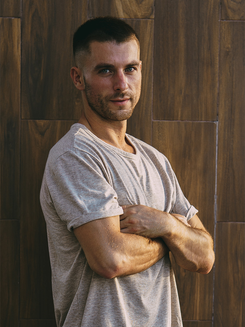 Confident man with crossed arms wearing casual gray t-shirt against wooden wall background - Urethral fistula repair in Clifton, NJ