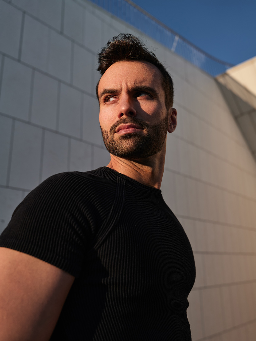 Man in black shirt taking selfie against modern white building with blue sky background - Urethral lengthening in Clifton, NJ