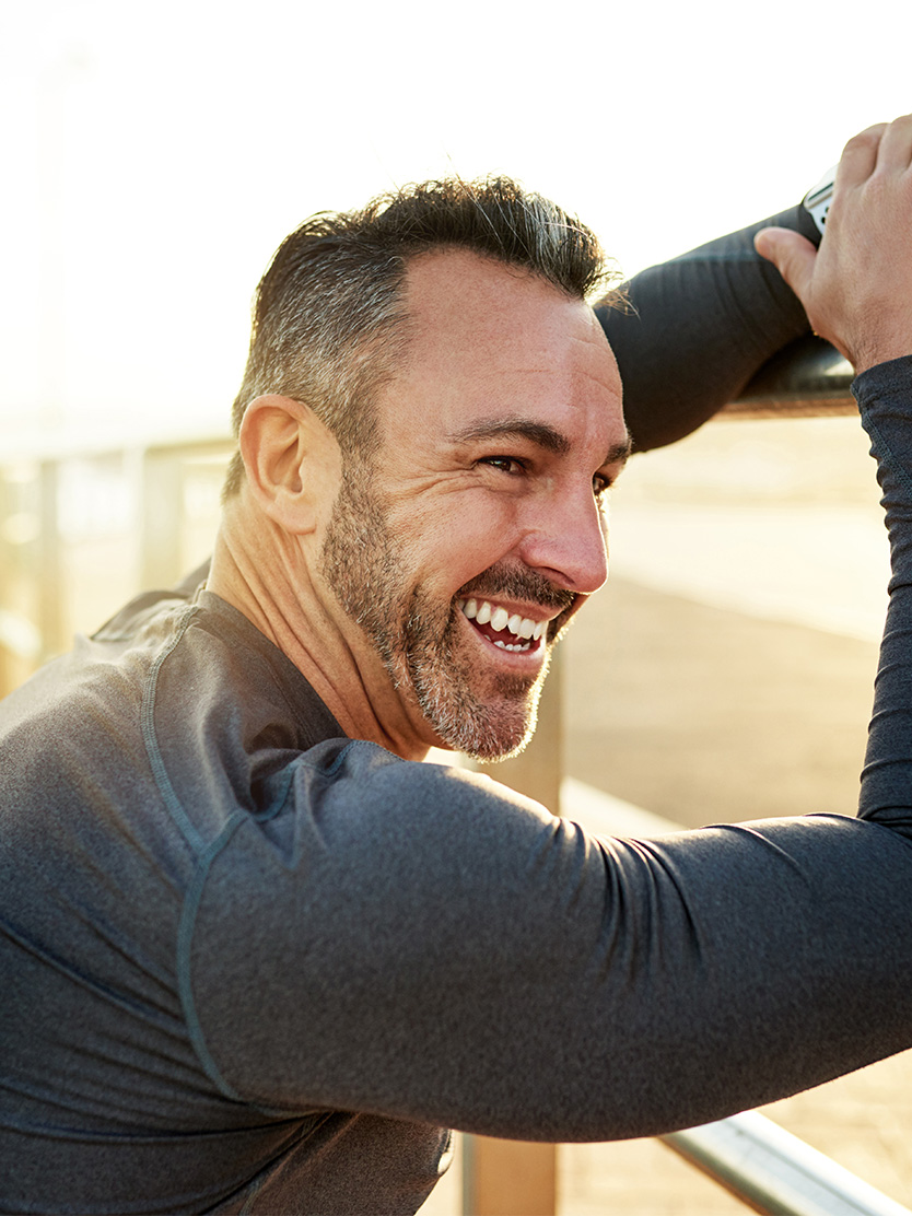 Happy middle-aged man smiling outdoors with hand in hair wearing gray athletic shirt - Urethral strictures in Clifton, NJ