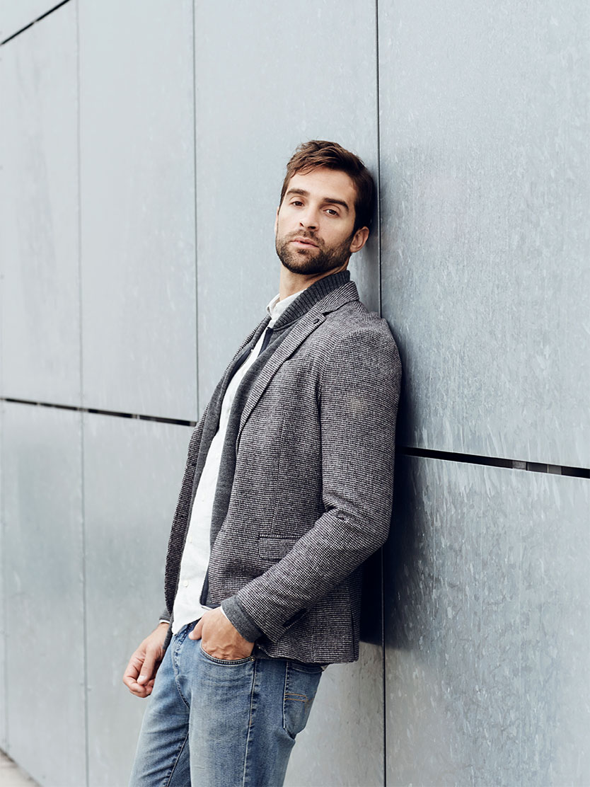 Man in gray blazer and jeans leaning against modern concrete wall in casual business attire - Urethroplasty in Clifton, NJ