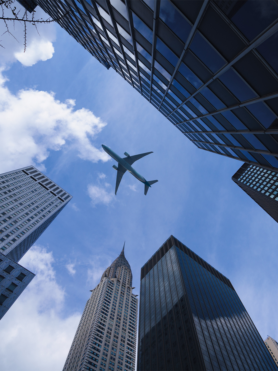 Airplane flying overhead between tall city skyscrapers against blue sky with clouds - arrival in Clifton, NJ