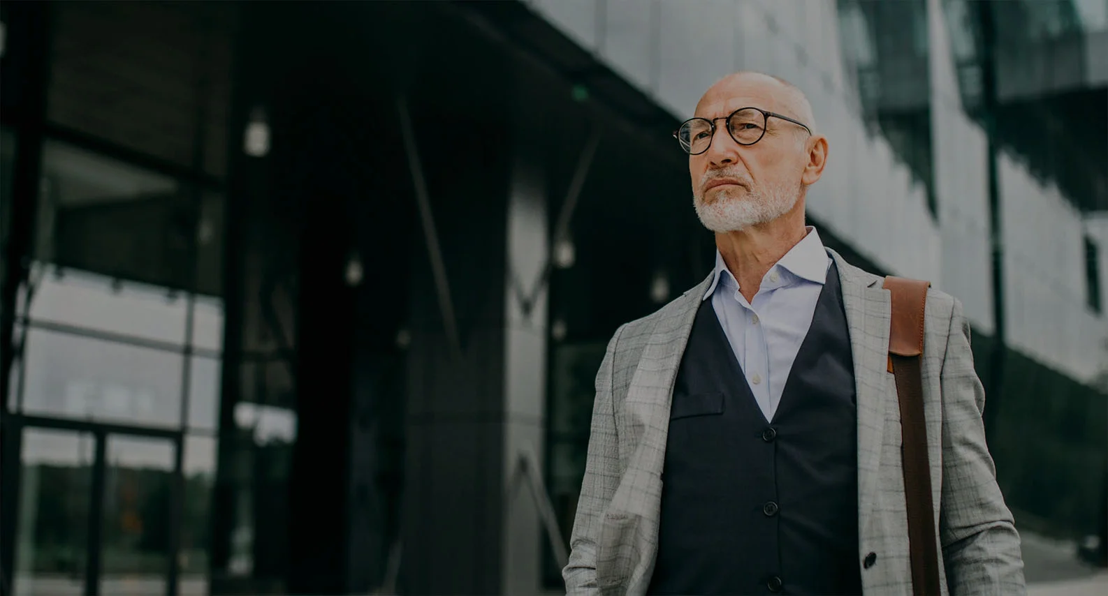 Distinguished senior businessman in vest and glasses standing confidently in modern office - in Clifton, NJ
